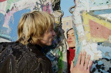 A couple blow a kiss to each other through the mural-covered remains of the Berlin Wall.