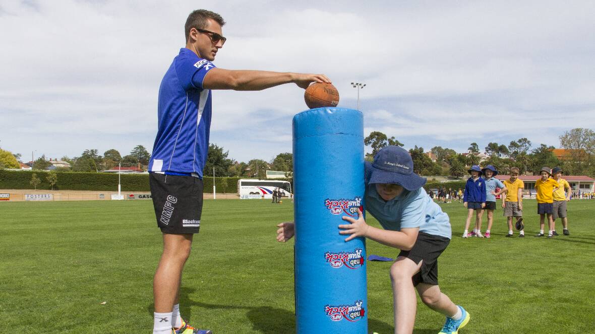 North Melbourne footballer Ben Jacobs runs Liam through a tackling drill. Picture: PETER PICKERING.