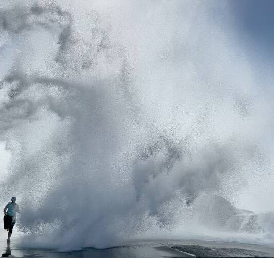 SPRAY JOB: A jogger tries unsuccessfully to outrun a wave breaking over Nobbys breakwall on Sunday. Watch the video at theherald.com.au. Picture: Jane Lynch