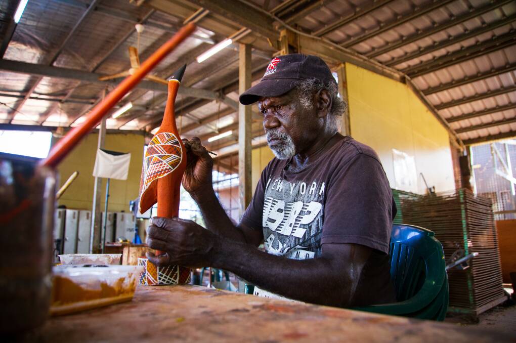 An artist works on a tutini, a carved and painted pole. Tourism NT/Felix Baker
