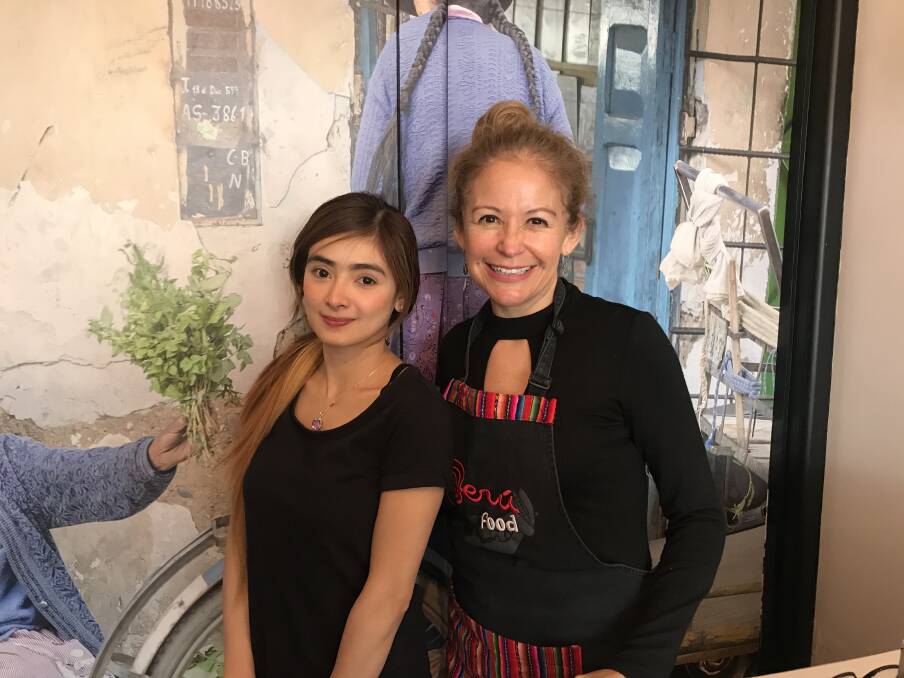 BACK TO BUSINESS: Mae Logan and Giovanna Monaghan infront of a mural of a scene from Mrs Monaghan's mother's home town, Huaraz, Peru at the Pachamama Cafe Stawell. Picture: CASSANDRA LANGLEY