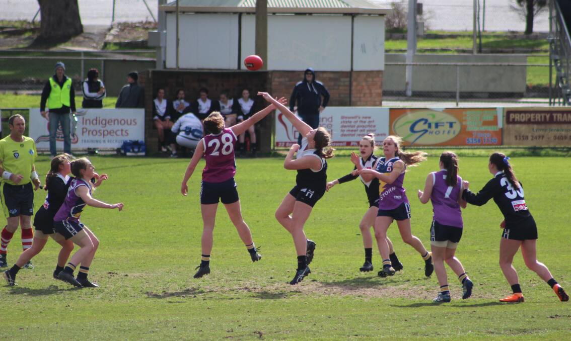Junior female footballers fly in a ruck contest. 